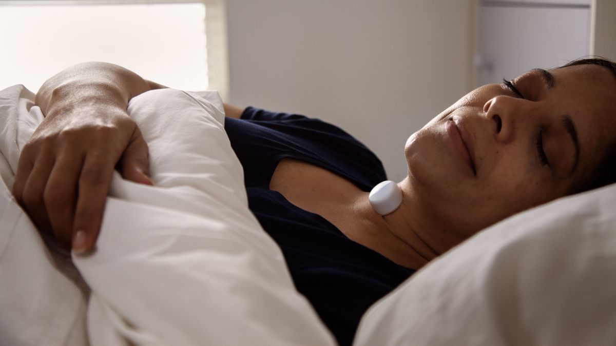 A woman lies in bed asleep with the Acurable AcuPebble obstructive sleep apnea detection device placed on the outside of her throat where it constantly detects symptoms