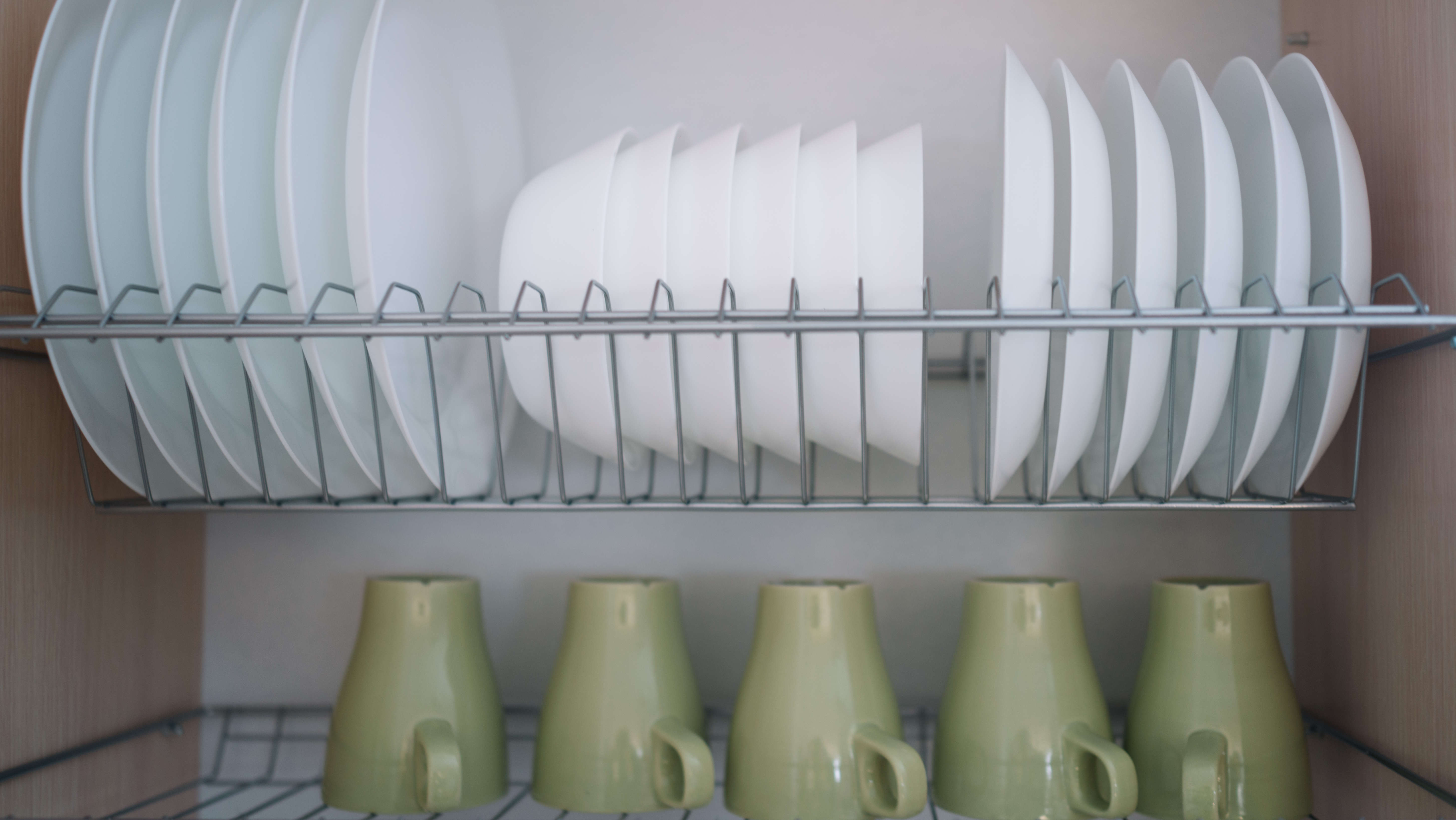 צלחות וספלים מאוחסנים על מדפי חוטים בארון המטבח