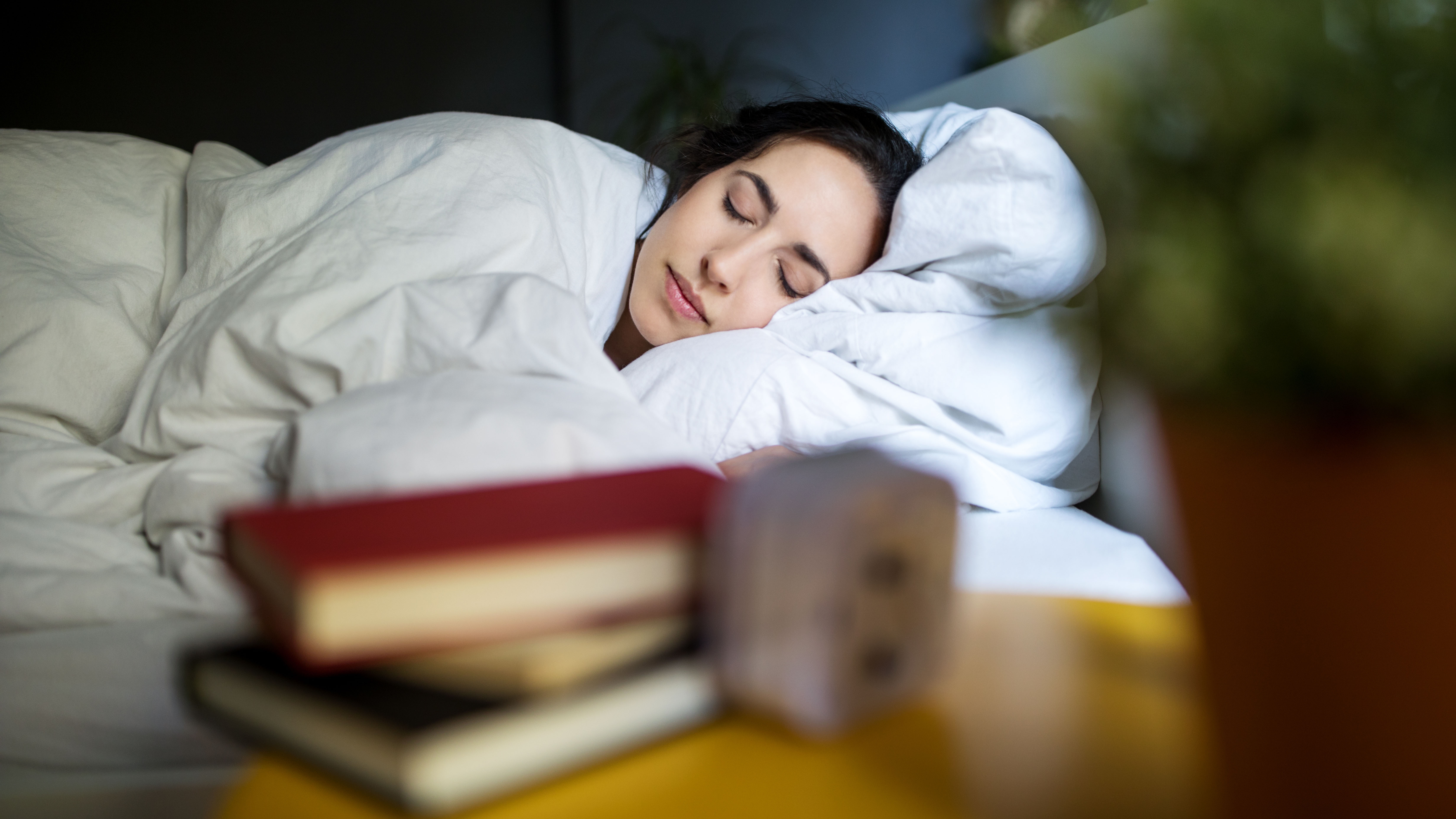 אישה ישנה בשלווה במיטתה מתחת לשמיכת פוך לבנה, בעוד ערימה קטנה של ספרים נראית על שולחן המיטה שלה