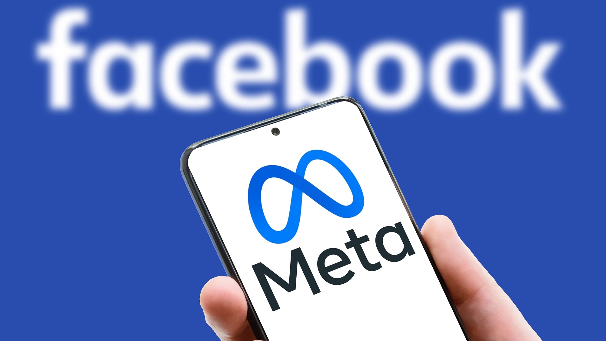 מטא לוגו על מסך הטלפון הנייד ברקע מילת פייסבוק.  פייסבוק לאחר מיתוג מחדש והחלפת שם ל-Meta.