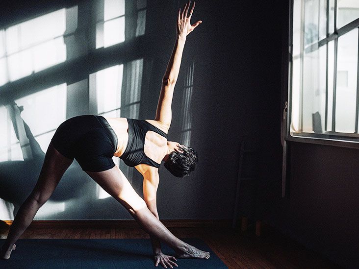 A woman stretches her back while doing yoga exercises near a window