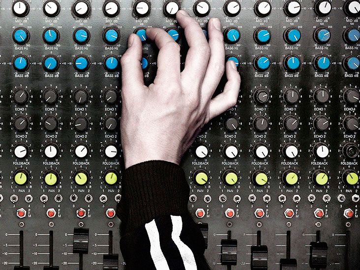 A hand turns up a knob on an audio board