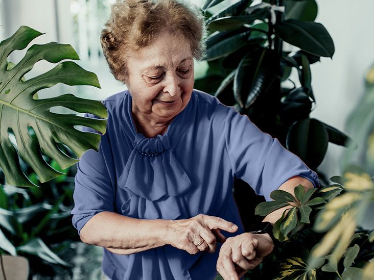 older woman surrounded by tall plants checking smartwatch