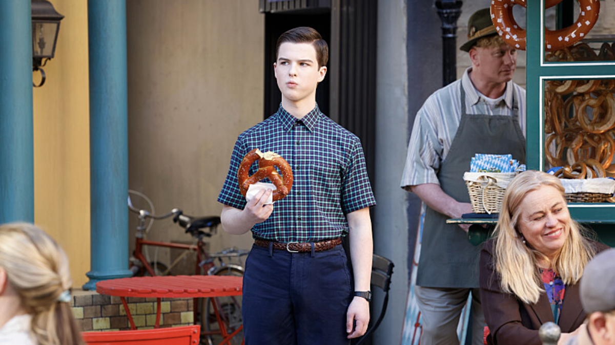 Sheldon Cooper (Iain Armitage) eating a pretzel outside a German cafe in