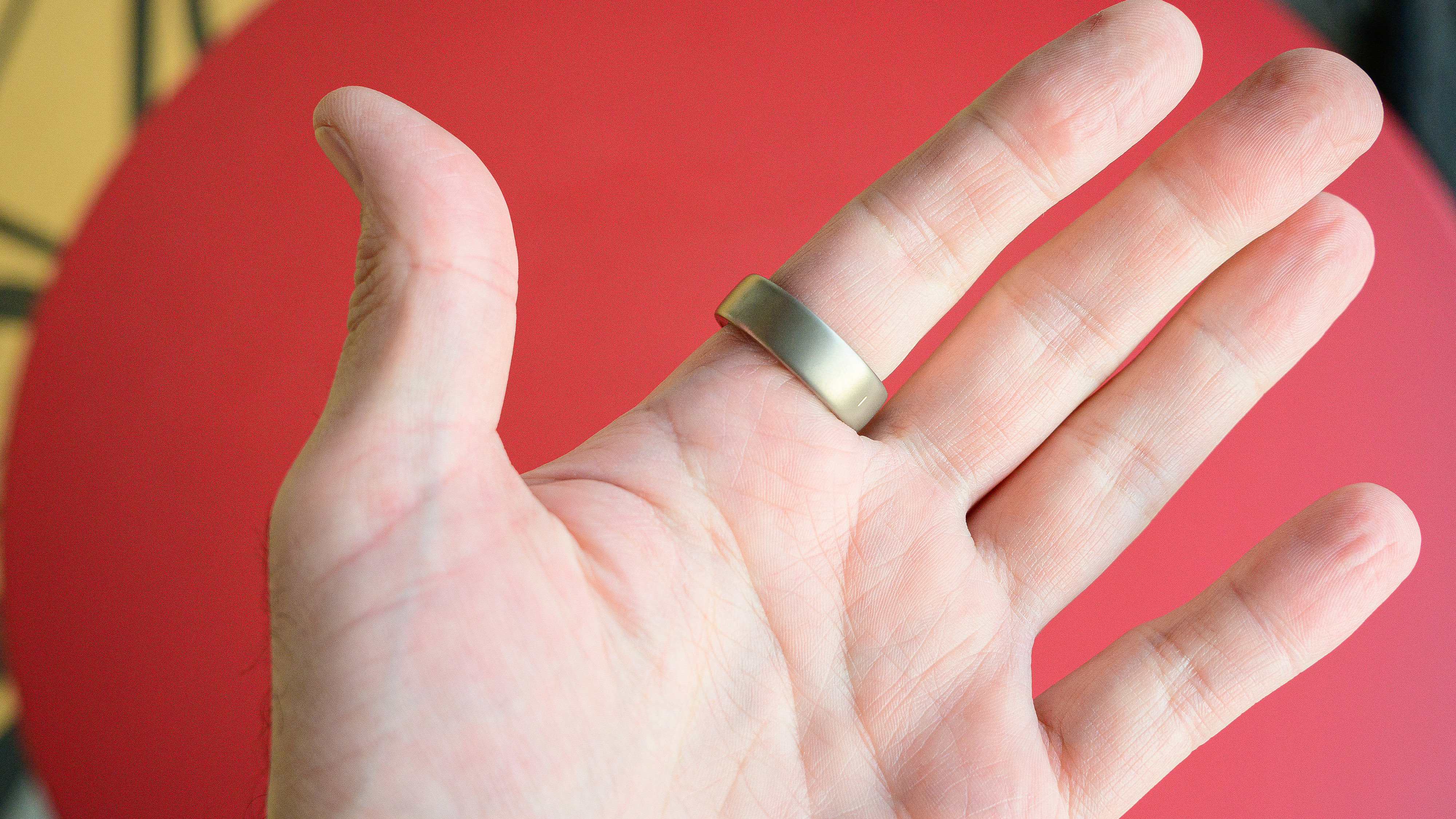 טבעת Amazfit Helio על אצבע של אדם עם רקע אדום מאחור