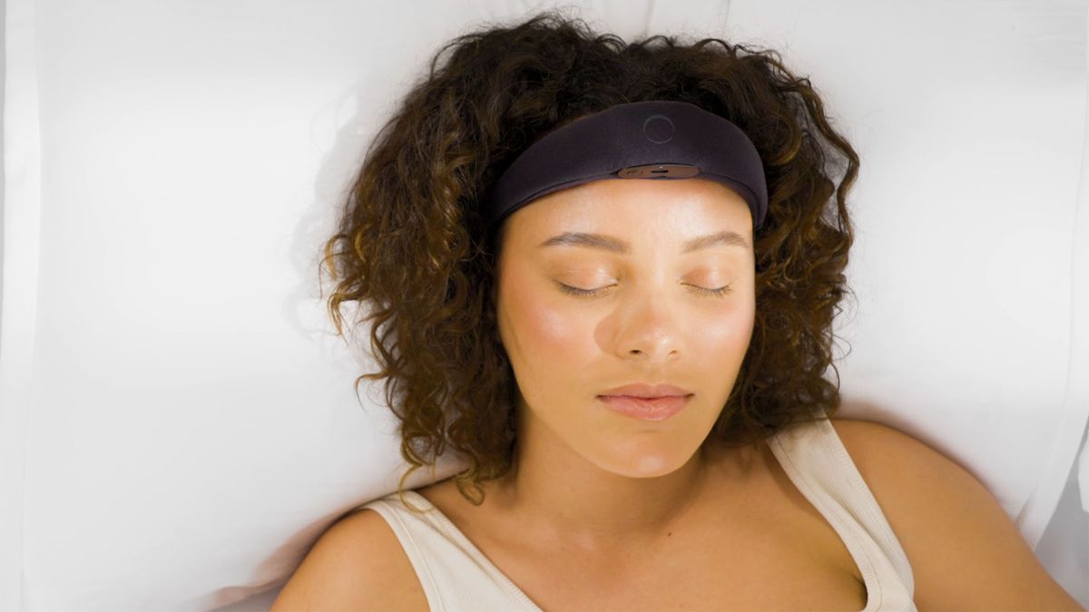 A woman lies in bed wearing the Elemind neurotech headband, she
