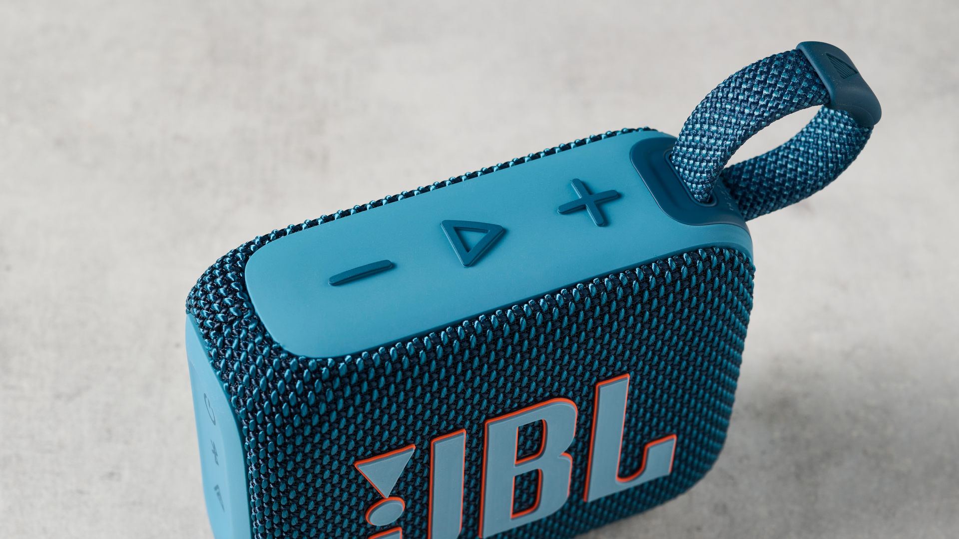 תמונה של ה-JBL Go 4 בכחול על משטח בטון על רקע קיר כחול.