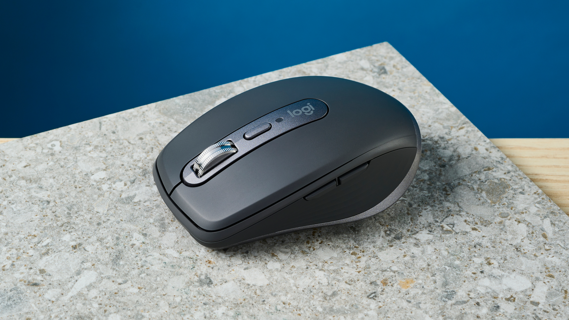 תמונה של עכבר Logitech MX Anywhere 3S על משטח אבן עם קיר כחול ברקע.