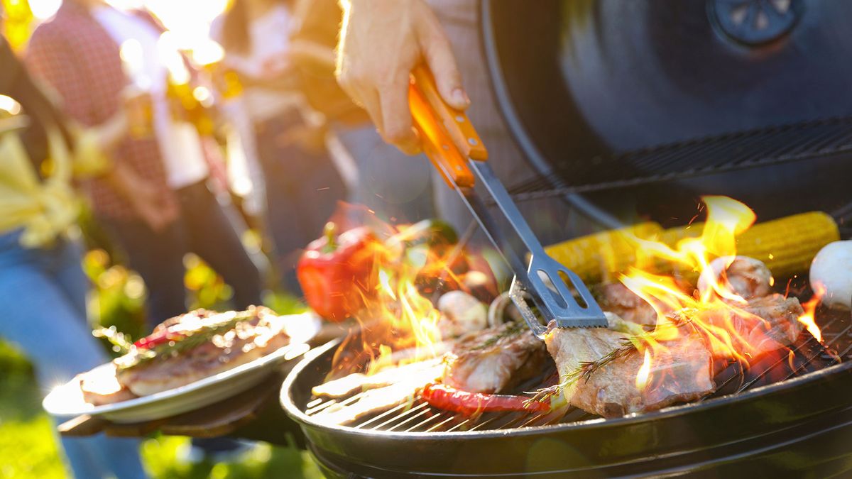 Food cooking on a grill with people socialising in background
