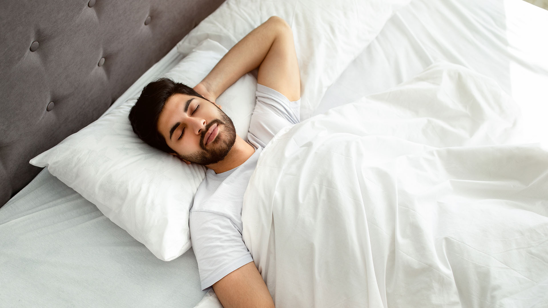 גבר שוכב על גבו במיטה, ישן בשמחה בתנוחה נוחה