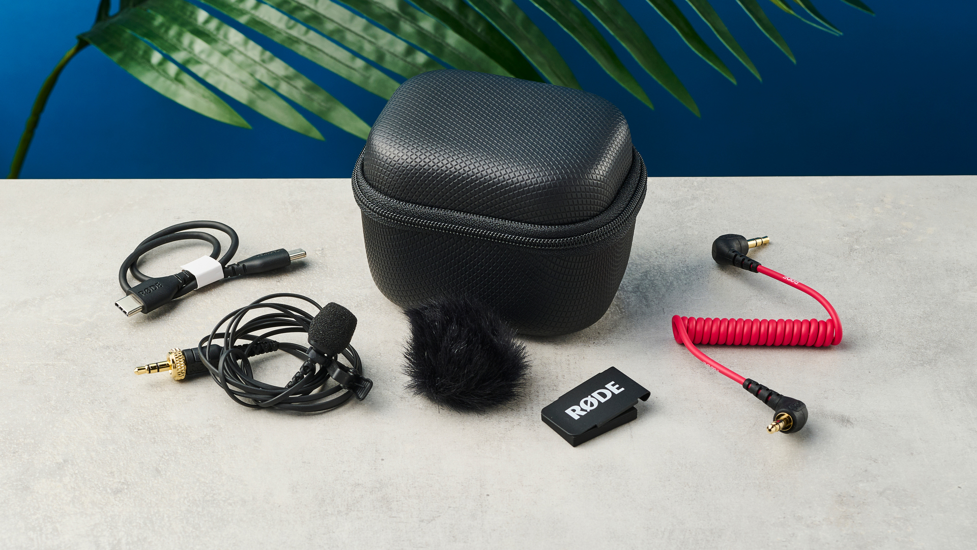 מיקרופון Rode Wireless Pro עם כל האביזרים שלו מונחים על משטח אבן עם קיר כחול ברקע