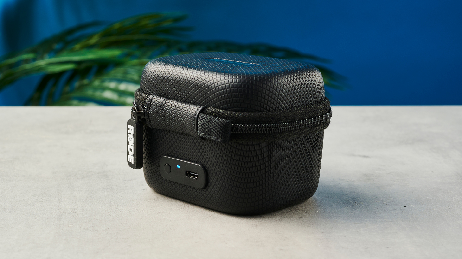 יחידות Rode Wireless Pro מיקרופון RX ו-TX במארז הטעינה הסגור שלהם עם קיר כחול ברקע