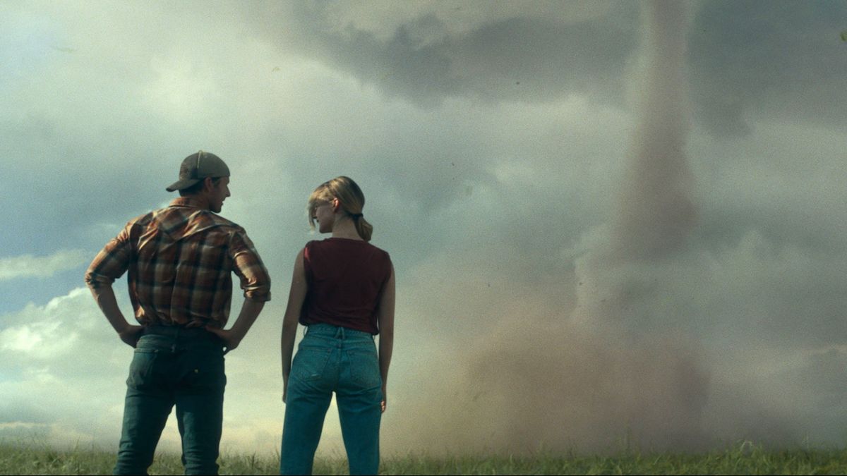 Glen Powell and Daisy Edgar-Jones facing away from the camera looking at a Tornado in