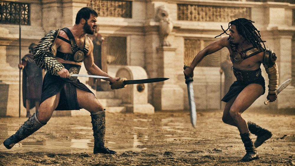 Viggo (Jóhannes Haukur Jóhannesson) and Kwame (Moe Hashim) decked out in gladiator gear as they face off in the arena in