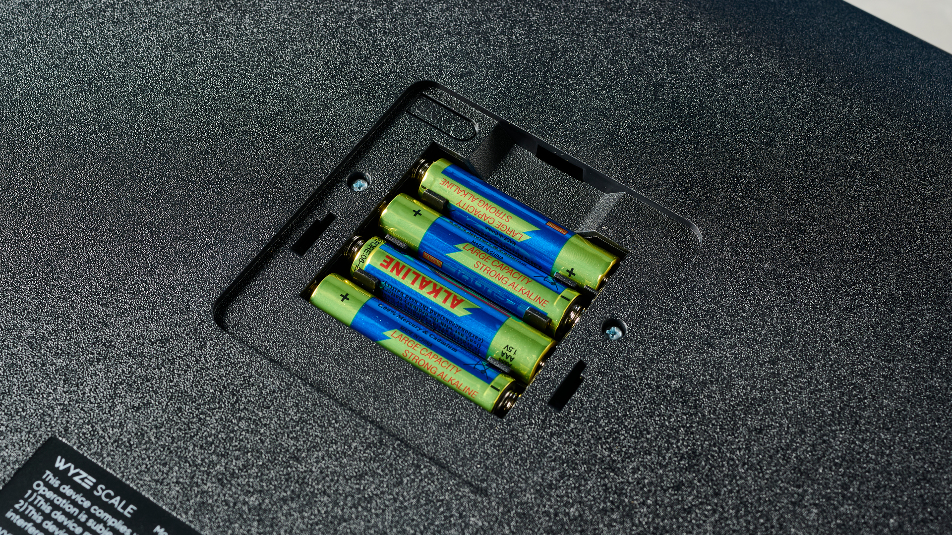 ארבע הסוללות בתוך משקל חכם מלוטש ונקי למראה עם גימור זכוכית מחוסמת ועיצוב בצורת צלב על גבי הזכוכית, כמעט כחול בתאורת הסטודיו, מונחת על שולחן