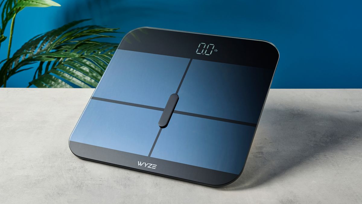 a close up picture of the wyze logo on a sleek, clean-looking smart scale with tempered glass finish and a cross-shaped design on top of the glass, almost blue in the studio lighting, rests upon a table