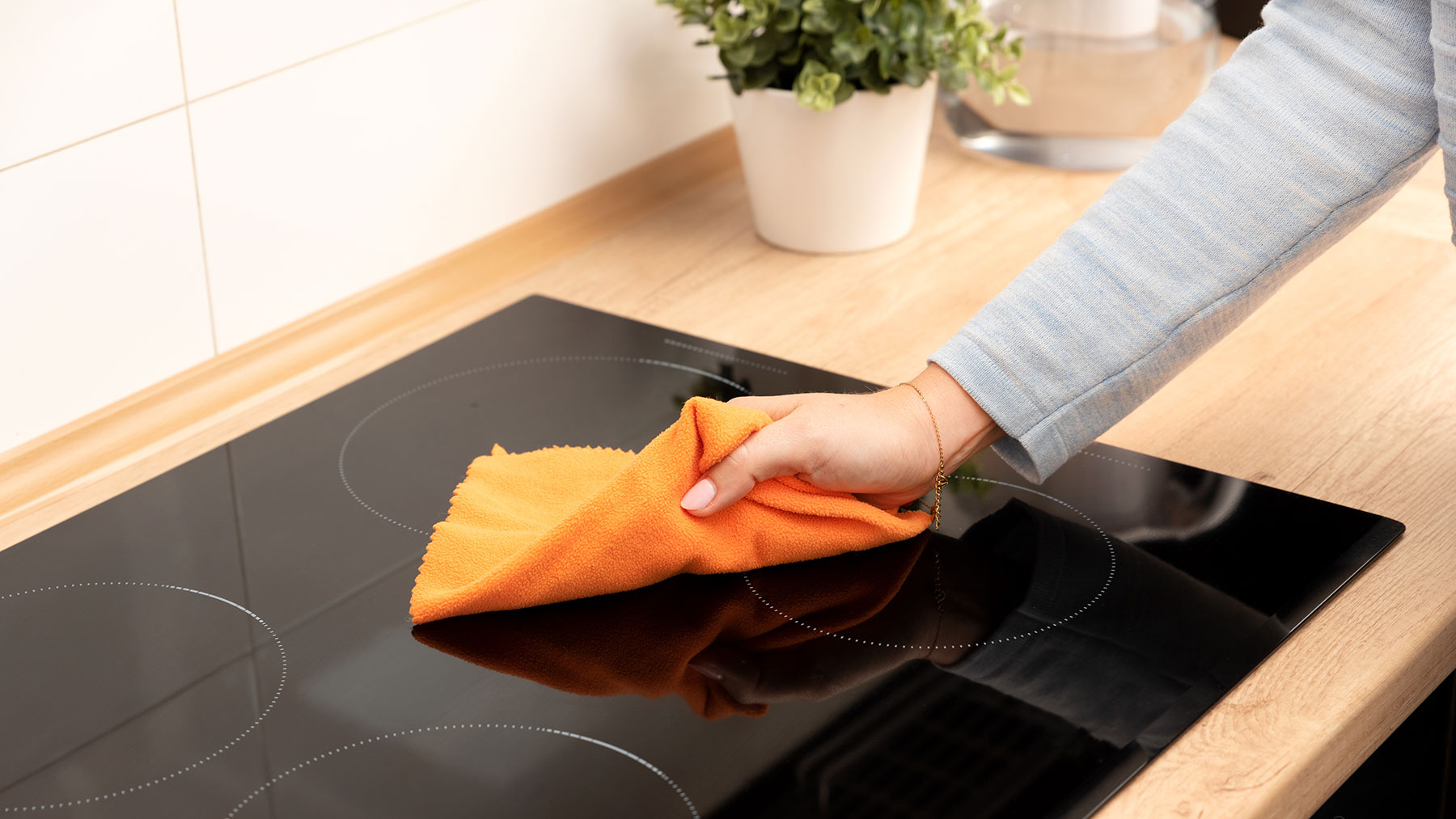 אישה מנקה כיריים אינדוקציה עם מטלית מעוטרת