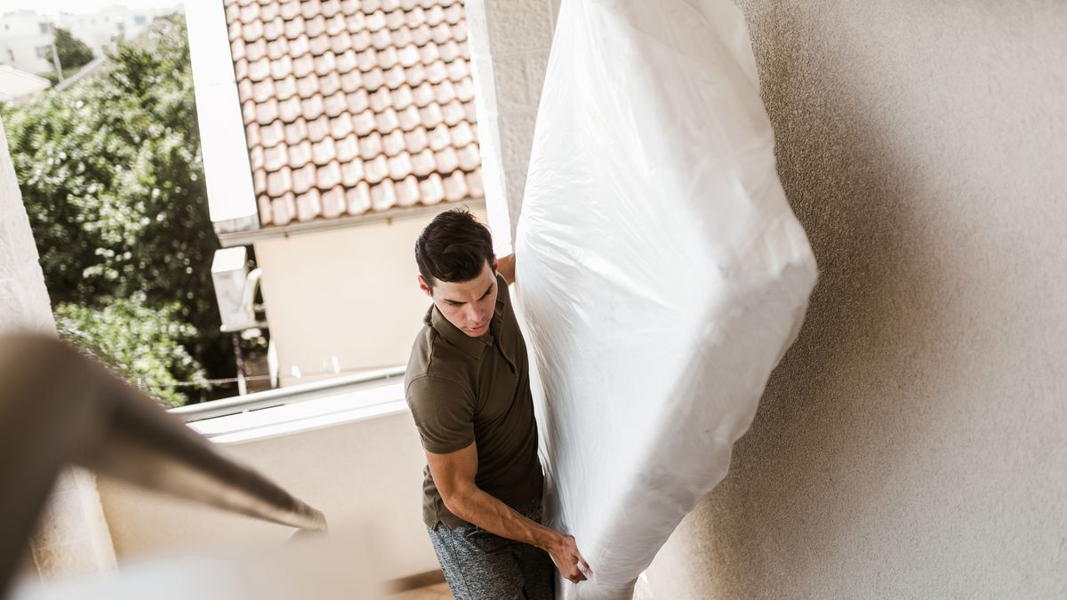 A man moves a mattress on his own up a flight of stairs