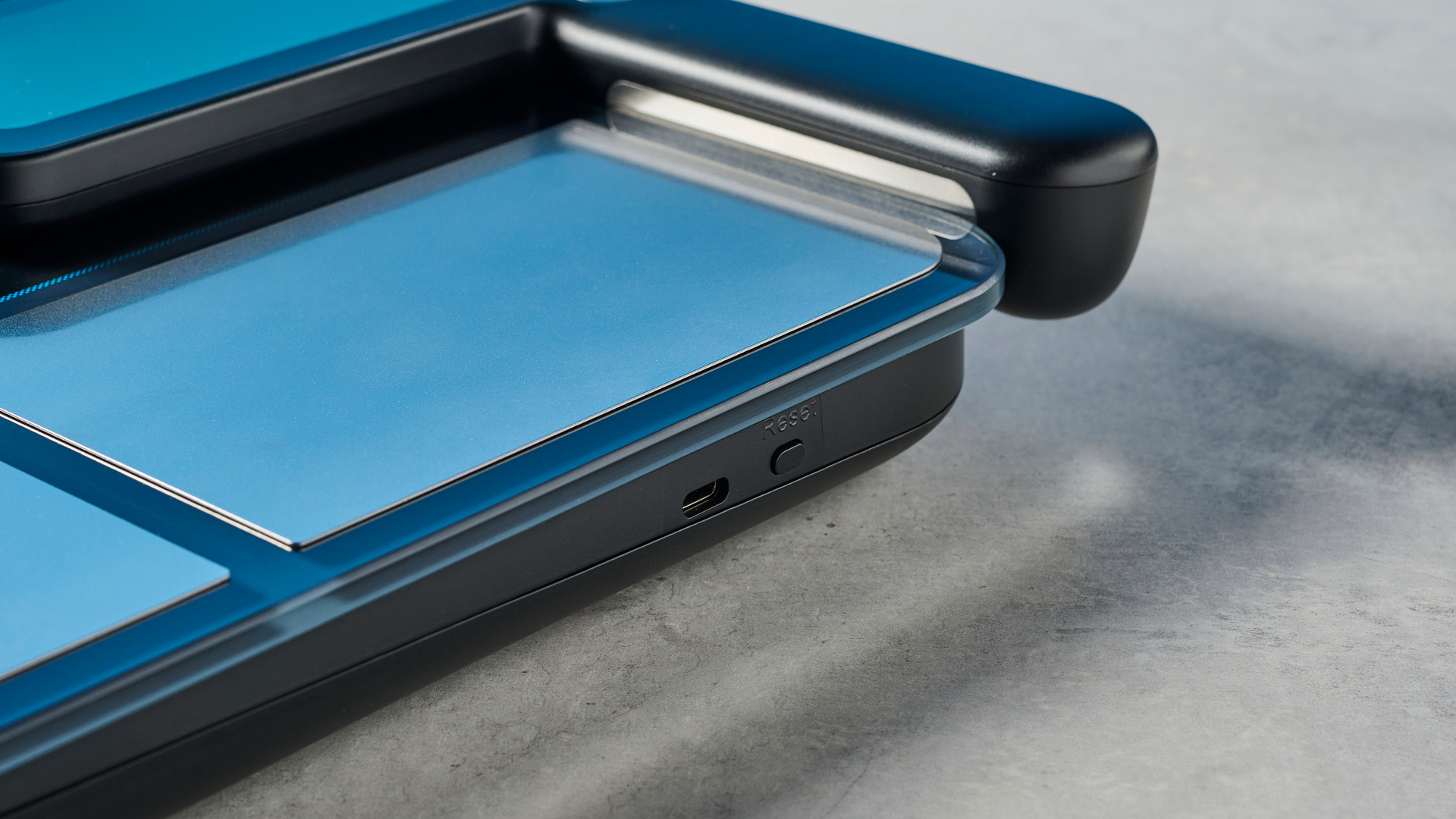 משקל חכם לשומן גוף של renpho עם ידית נשלפת למדידת אחוזי שומן בגפיים ואלקטרודות כסף ומעטפת כחול ושחור מונח על משטח מול רקע כחול