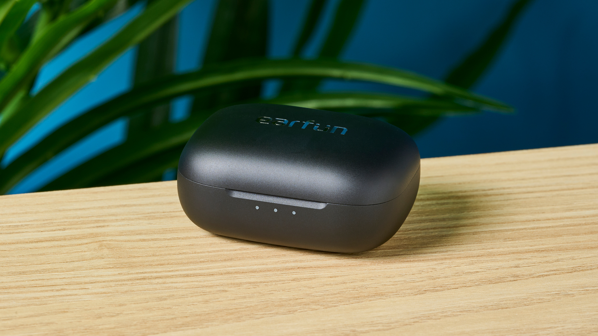 תמונה של נרתיק האוזניות EarFun Air Pro 4, סגור על משטח עץ עם קיר כחול ברקע
