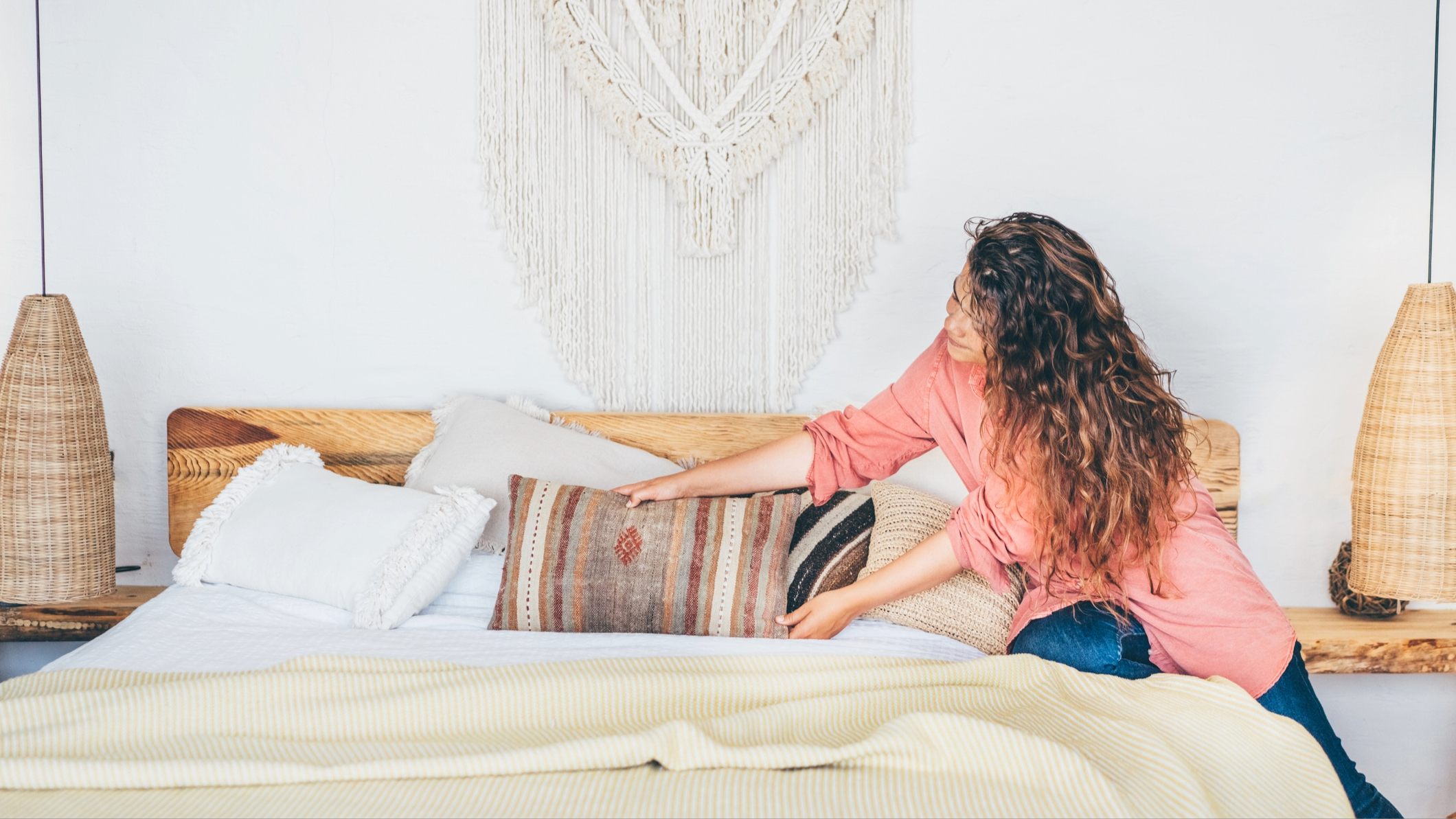 אישה מניחה כרית על מיטה מסודרת עם הרבה שכבות של מצעים