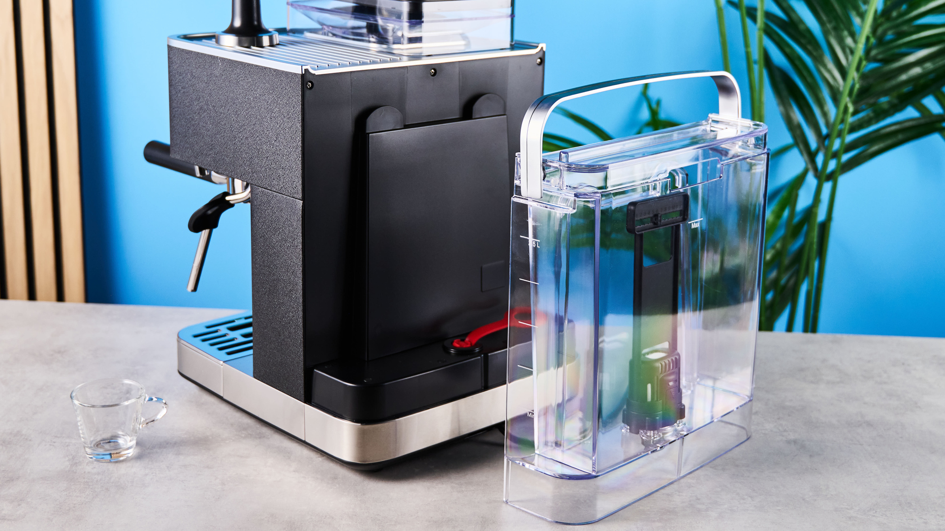 מכונת אספרסו שחורה של kitchenaid מצולמת על רקע כחול עם כפתורי כרום כסופים וחוגת לחץ ומטה קיטור