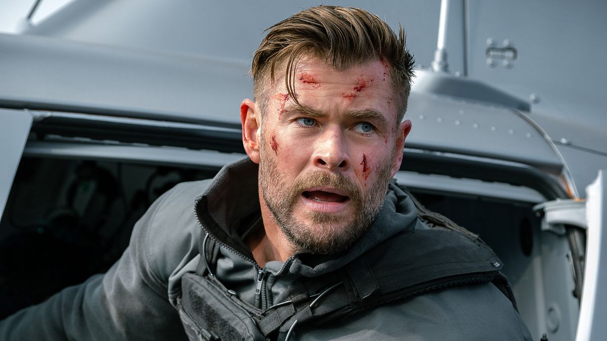 Chris Hemsworth, bruised, leans out of a helicopter in Extraction 2