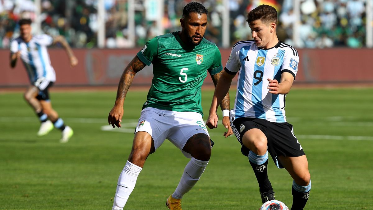 Julian Alvarez (R), in a blue and white striped shirt and black shorts, looks to keep the football from Adrián Jusino, wearing a green shirt and white shorts, during Argentina vs Bolivia.