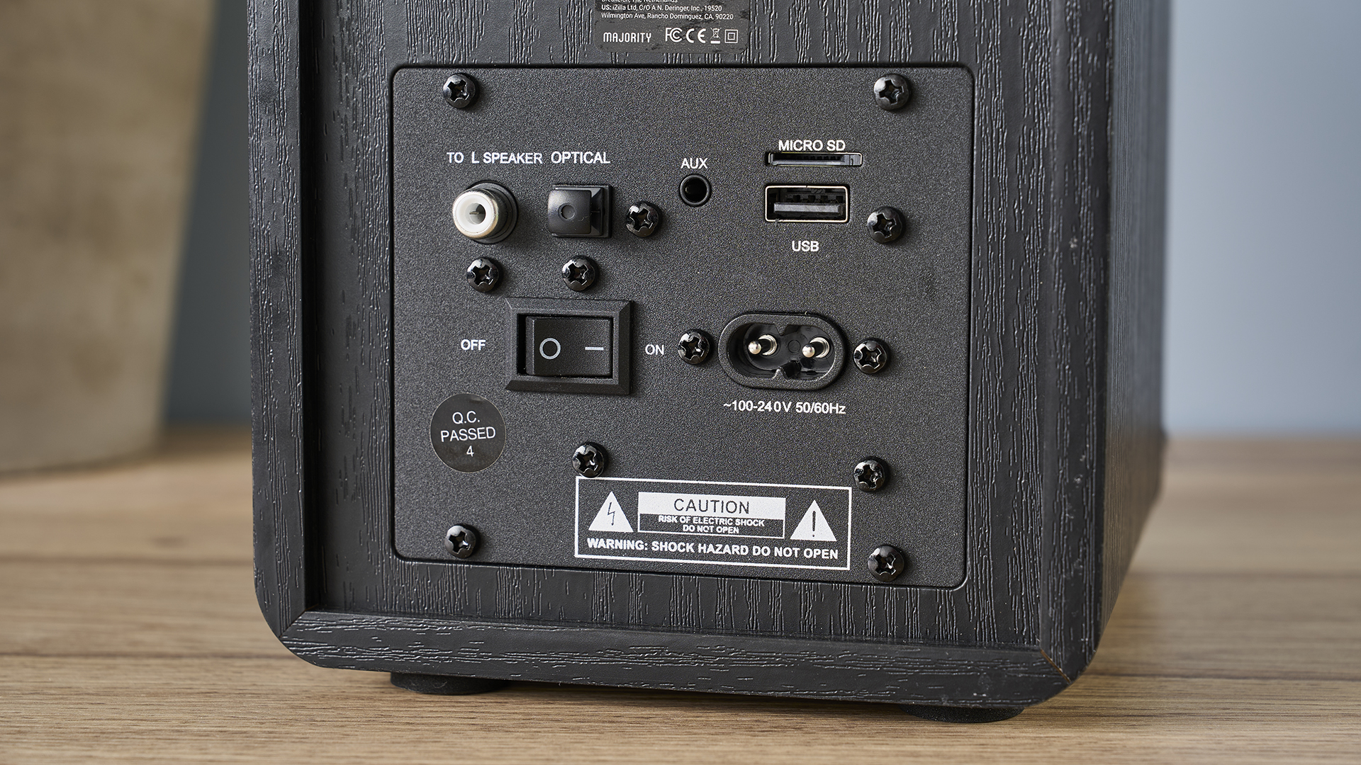 זוג רמקולים מעץ שחור עם חרוט קבלר צהוב צולם על שולחן עץ עם מחשב וקיר כחול וצמח בצילום