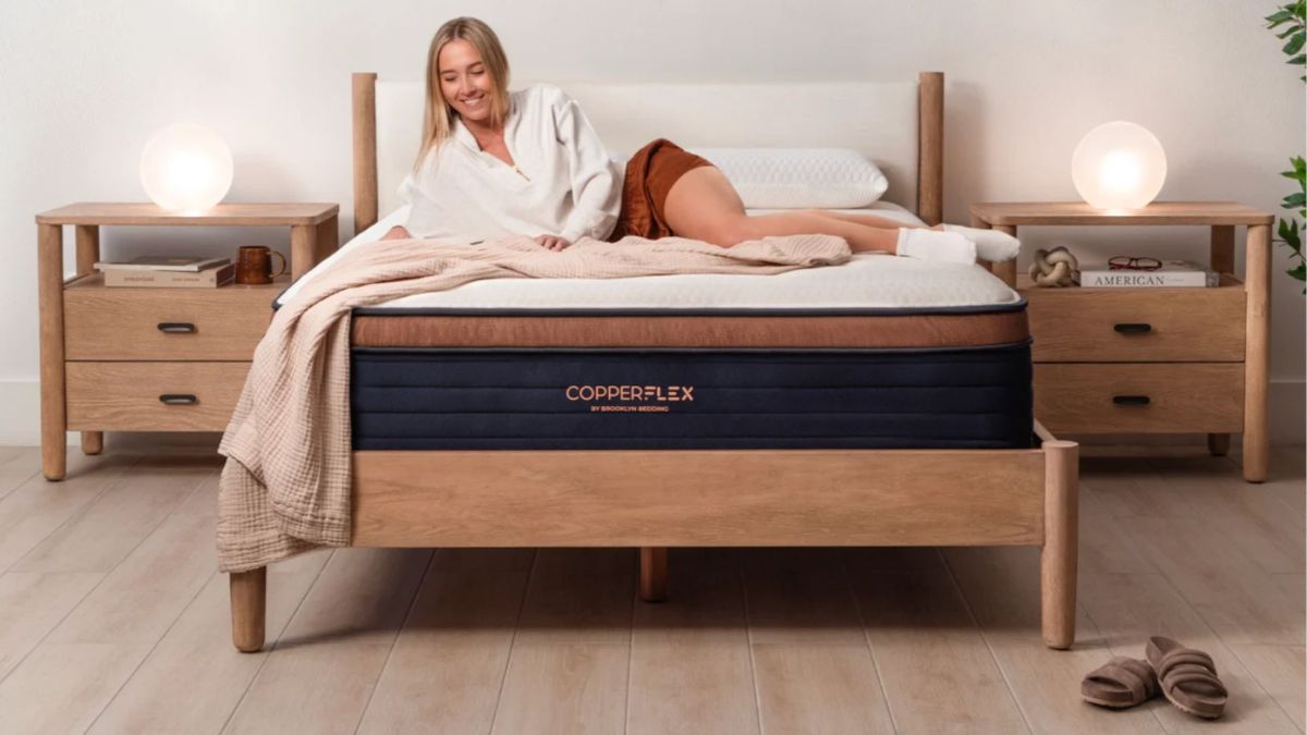 Blonde woman laying on Brooklyn Bedding CopperFlex mattress in bedroom with wooden floor, wooden bed base and two bedside tables