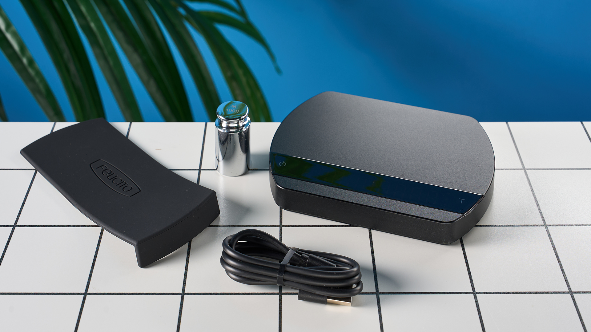 משקל קפה יוקרתי מתוצרת Felicita Arc מצולמת על רקע כחול עם משקלו, כבל USB-C ומחצלת סיליקון