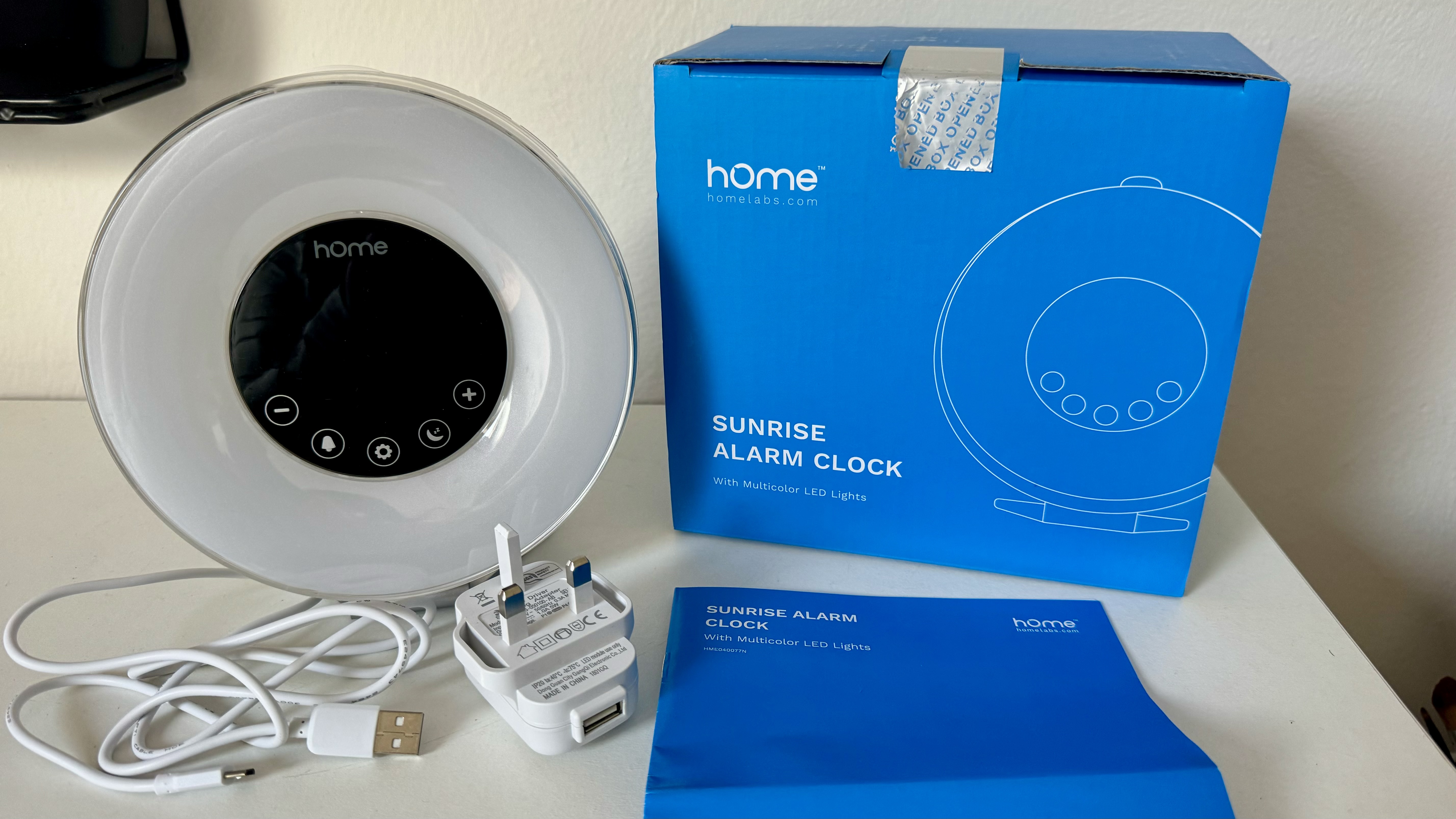 שעון מעורר של hOmeLabs Sunrise ללא ארגז לצד תקע וכבל לבנים, מדריך הוראות כחול וקופסה כחולה.