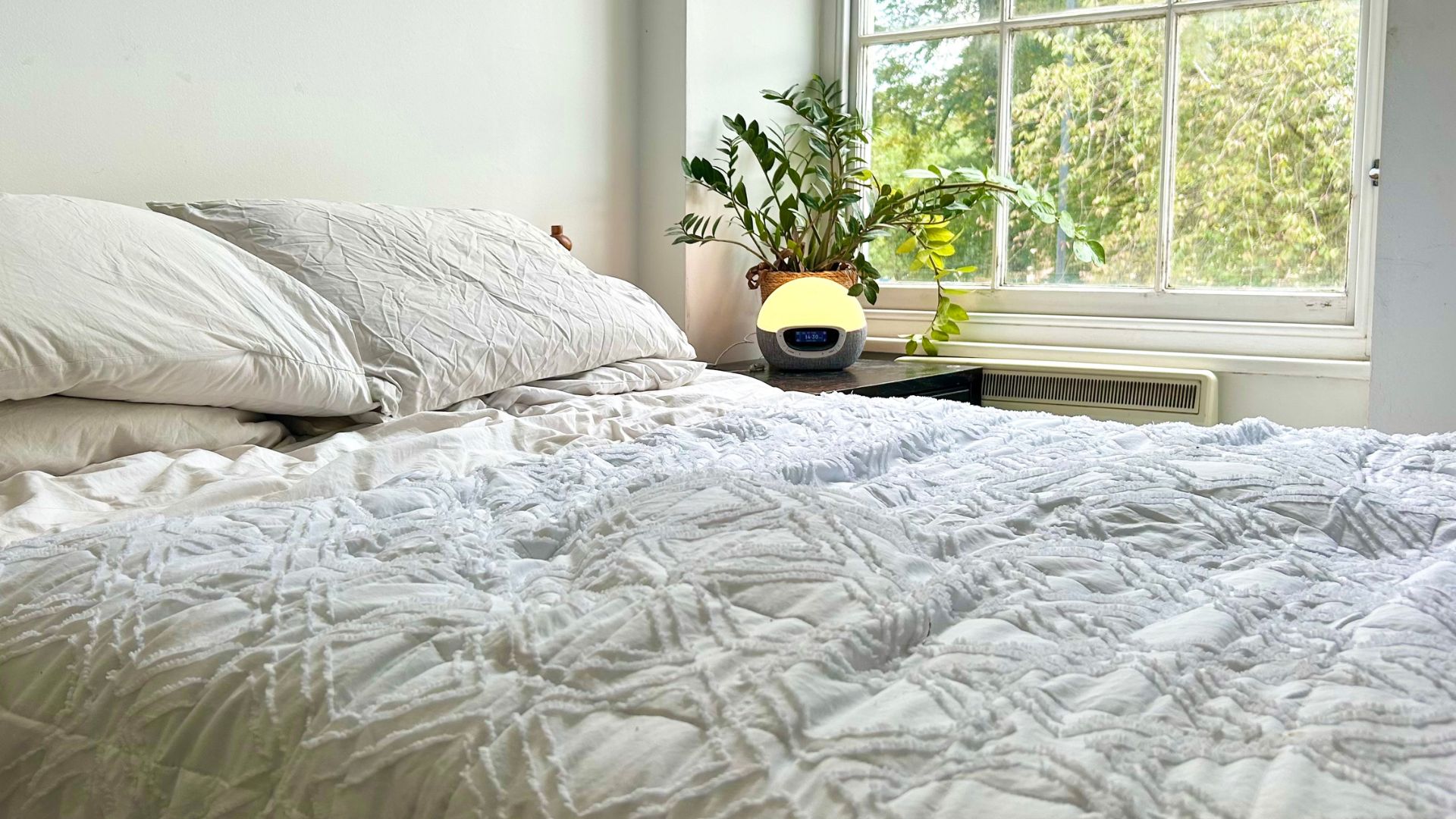 אור Lumie Bodyclock Shine 300 על שולחן המיטה ליד מיטה מול חלון פתוח