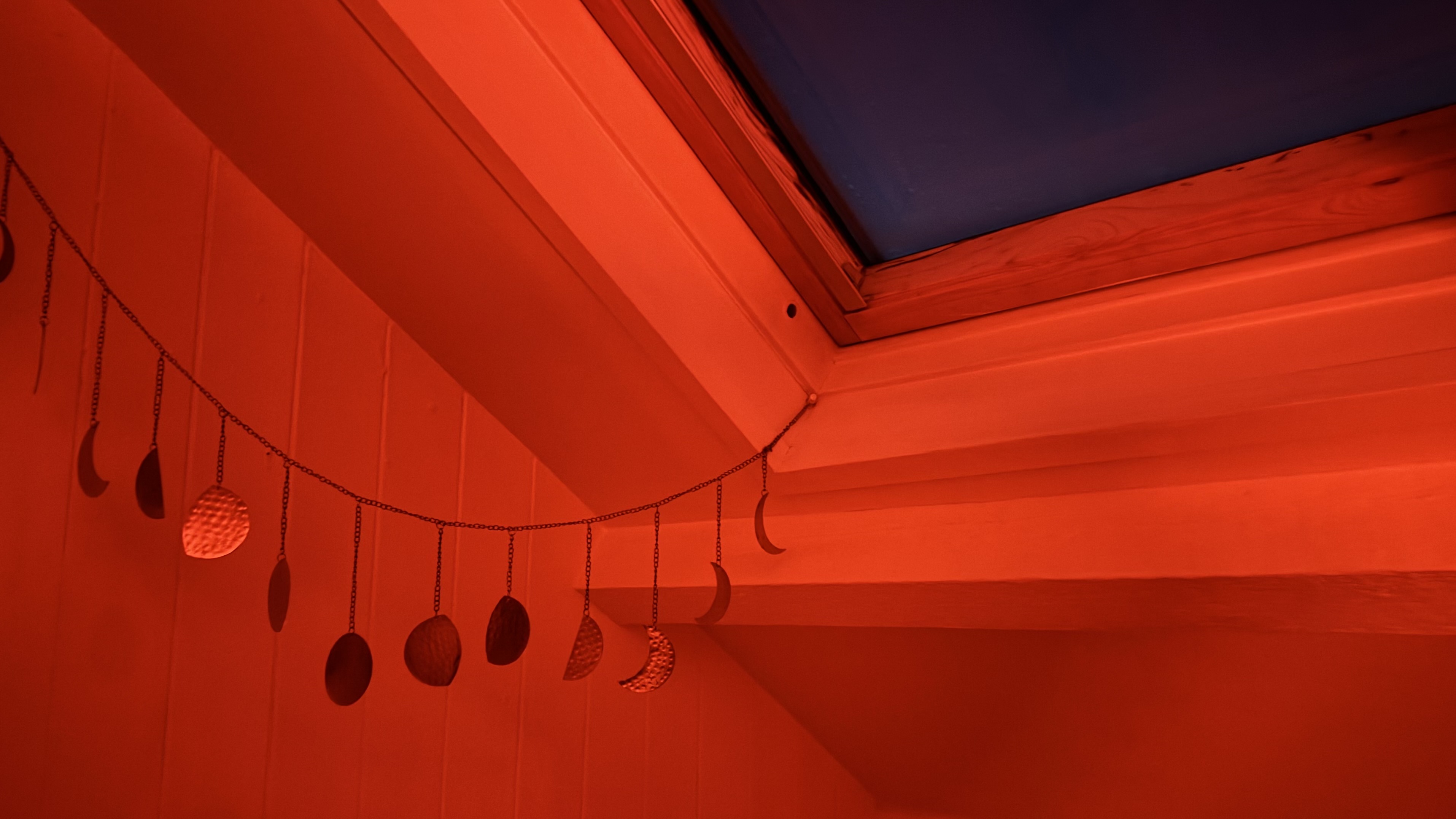 חלון חדר שינה בעליית גג. בוקר חשוך בחוץ. החדר מואר באור אדום משעון הזריחה.