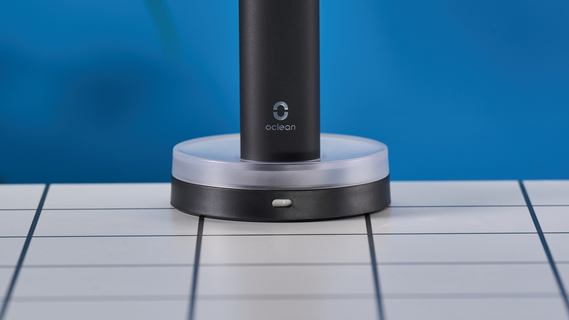 מברשת שיניים חשמלית שחורה עם מסך מגע קטן וראש מברשת שיניים כחול ומעמד טעינה מרובע