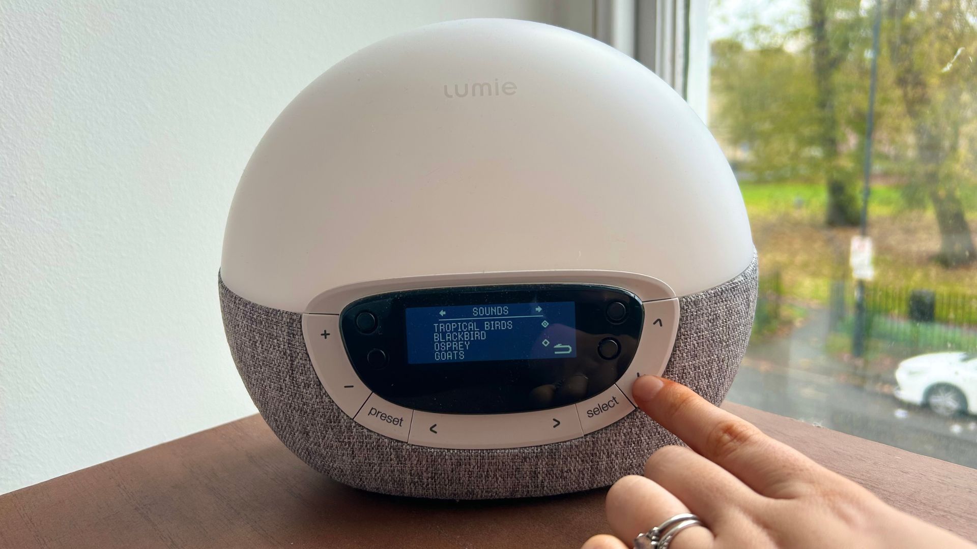 יד לוחצת על כפתור ב- Lumie Bodyclock Shine 300 המציגה את אפשרויות הסאונד השונות על המסך.