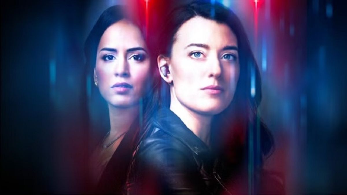 A red and blue police-inspired color motif surrounds a medium shot of Sunny, played by Agam Darshi, beside detective Tess Avery, played by Dolly Lewis in a press image for "Sight Unseen" season 2.