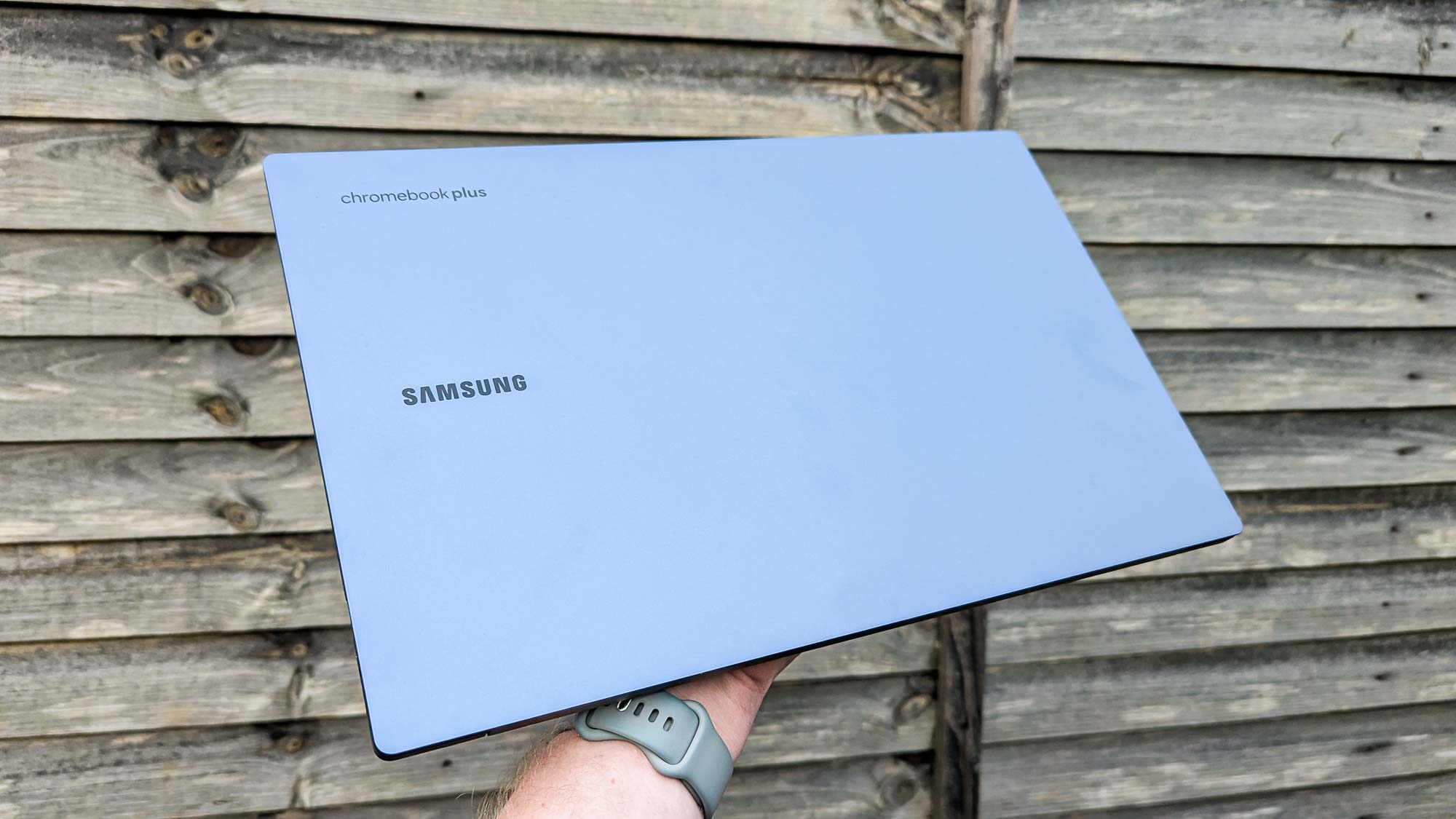 Samsung Galaxy Chromebook Plus סגור מוחזק ביד מול גדר עץ