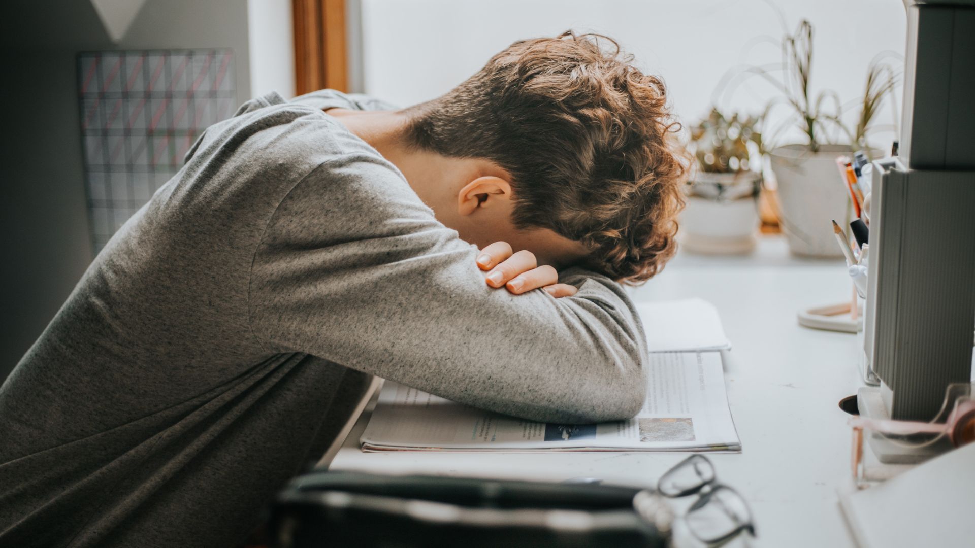 ילד מתבגר עם ראשו בזרועותיו ישן על ספר בזמן שהוא לומד