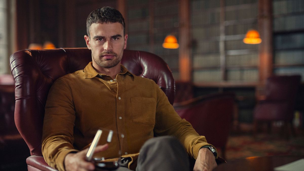 Eddie Horniman (Theo James) sits in a red armchair, with a glass of red wine in hand in Netflix's "The Gentlemen"