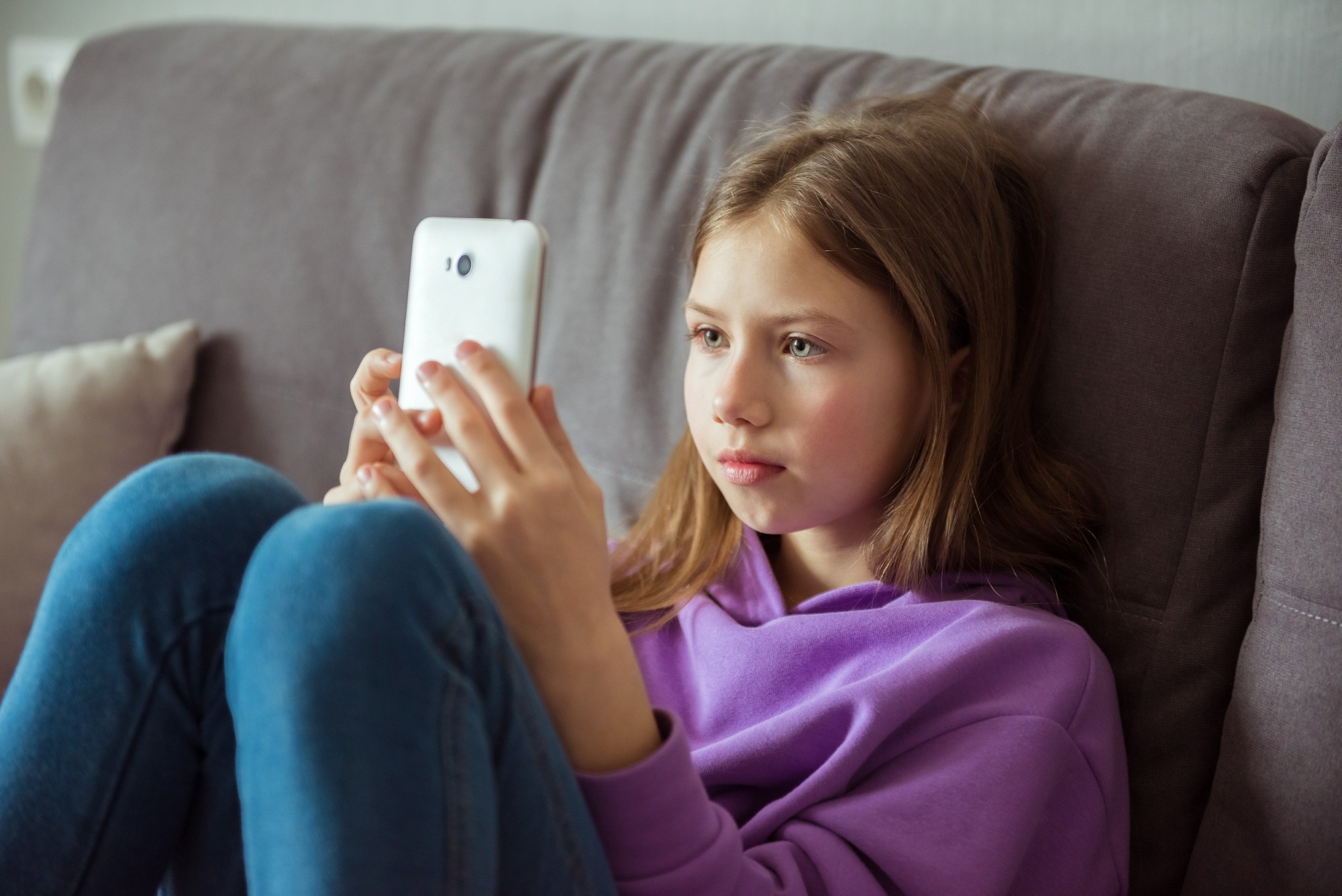 Upset depressed caucasian little kid girl holds mobile phone expresses sorrow and regret blames.