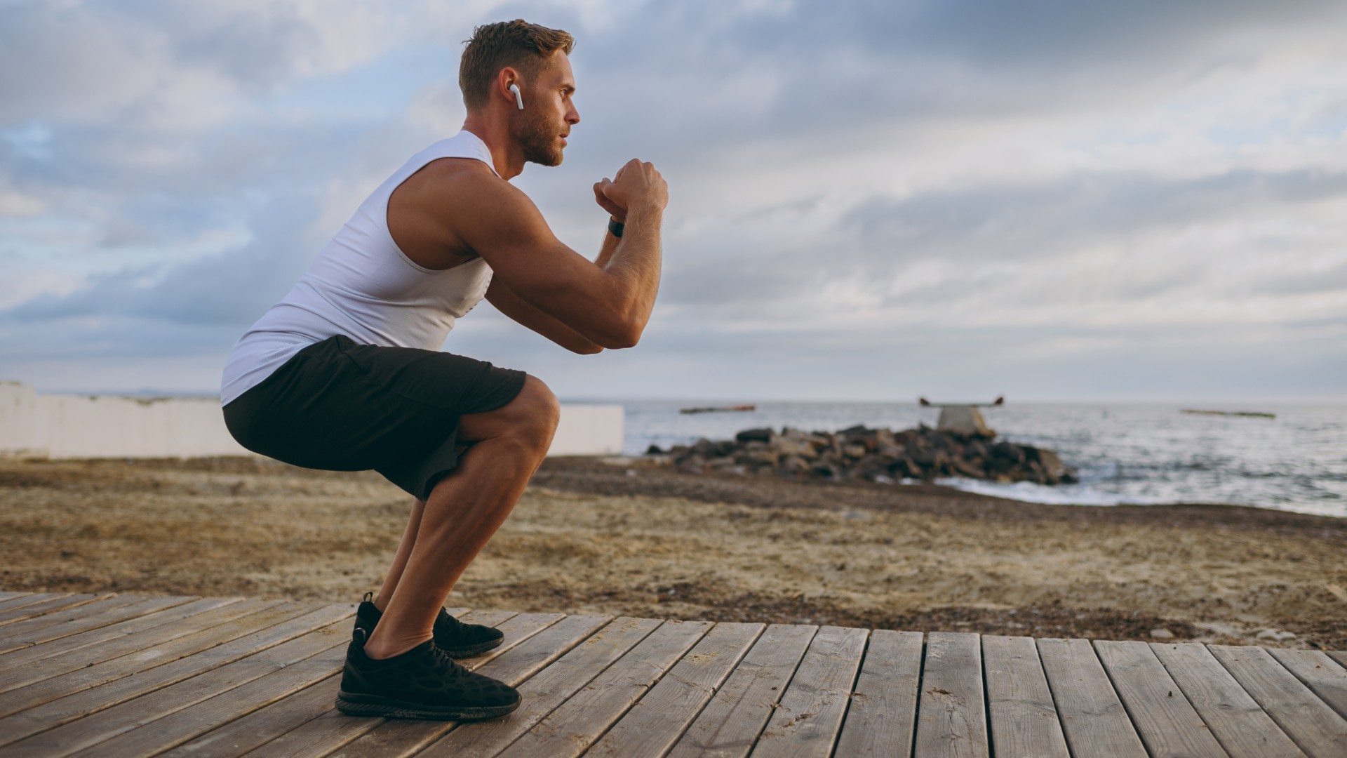 אדם מבצע את Squat משקל גוף בחוץ ליד האוקיאנוס במהלך אימון בחוץ