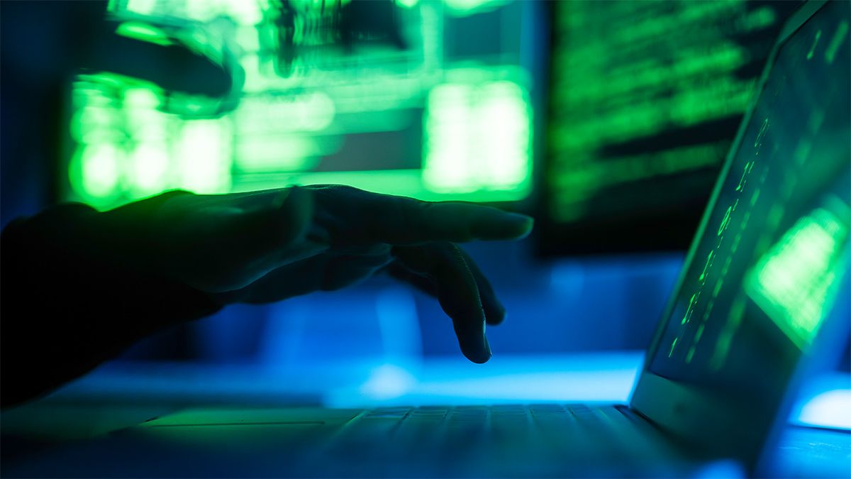 Hacker typing on laptop in darkened room