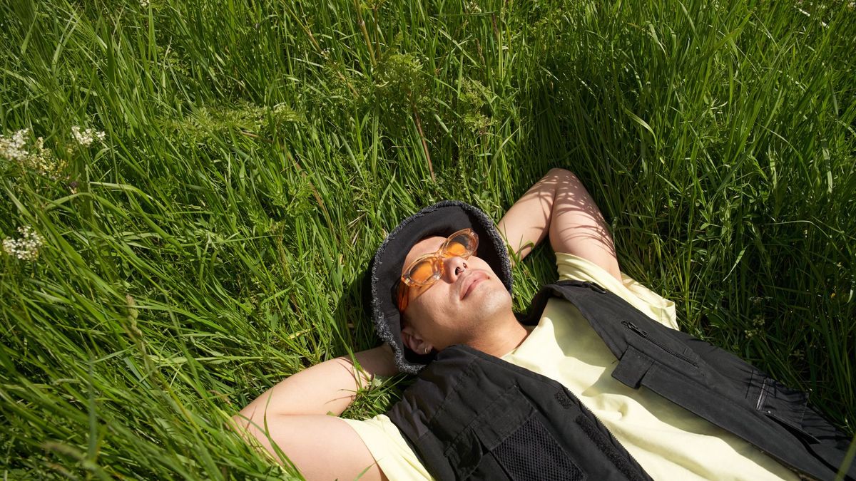 A man sleeping with his hands behind his head smiling on long grass