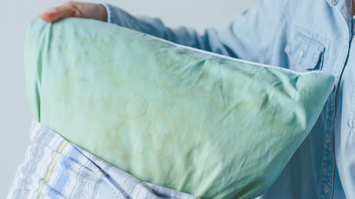 A person taking blue stained pillow with yellow patched out from a printed pillow case