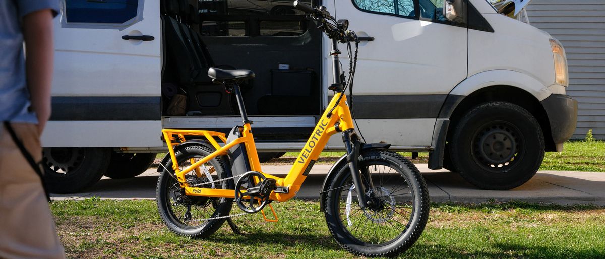 Velotric Fold 1 Plus ebike outdoors in front of white van on grass