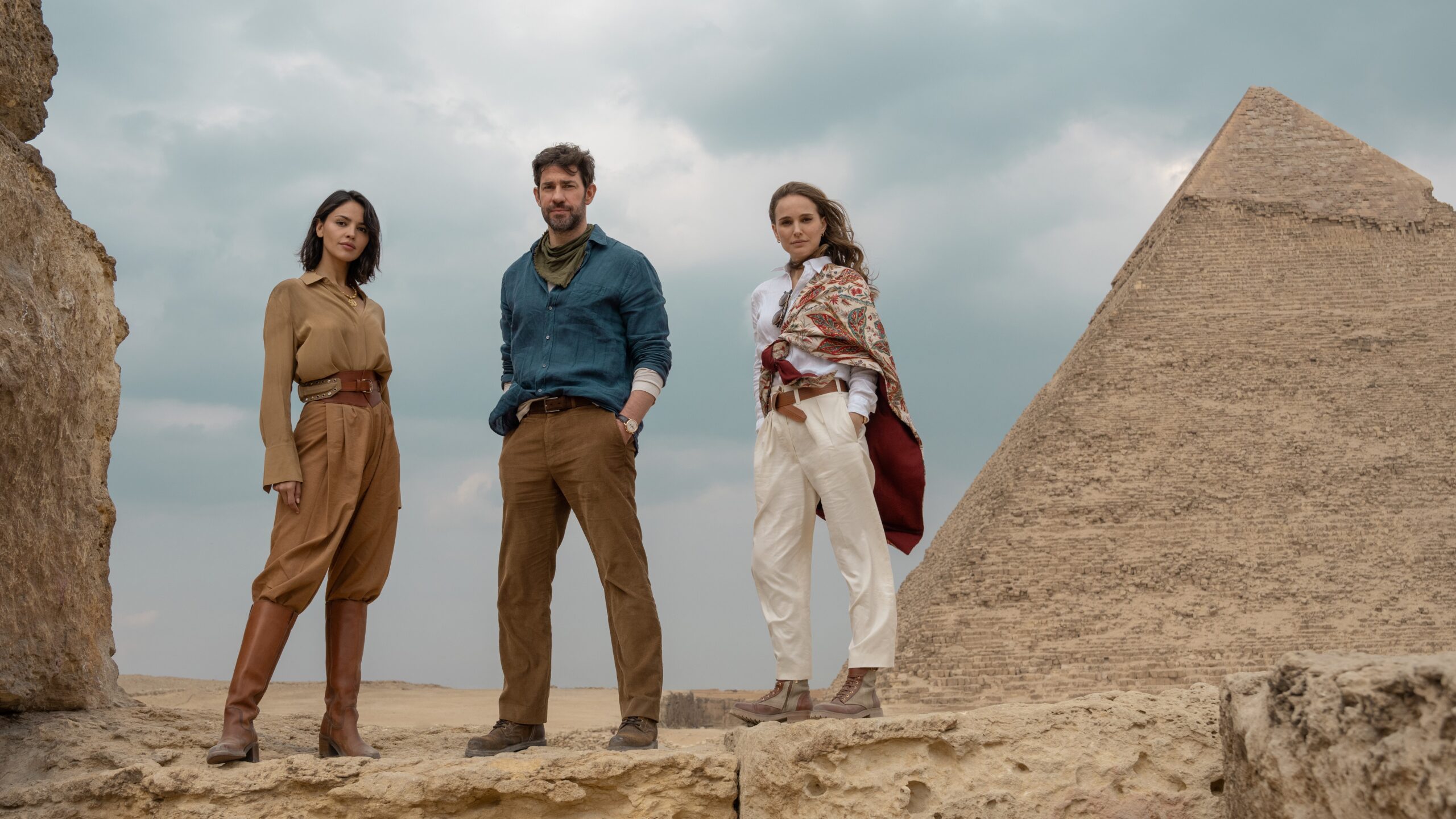 Eiza Gonzalez, John Krasinski and Natalie Portman (L-R) standing next to a pyramid in Apple TV Plus' "Fountain of Youth"
