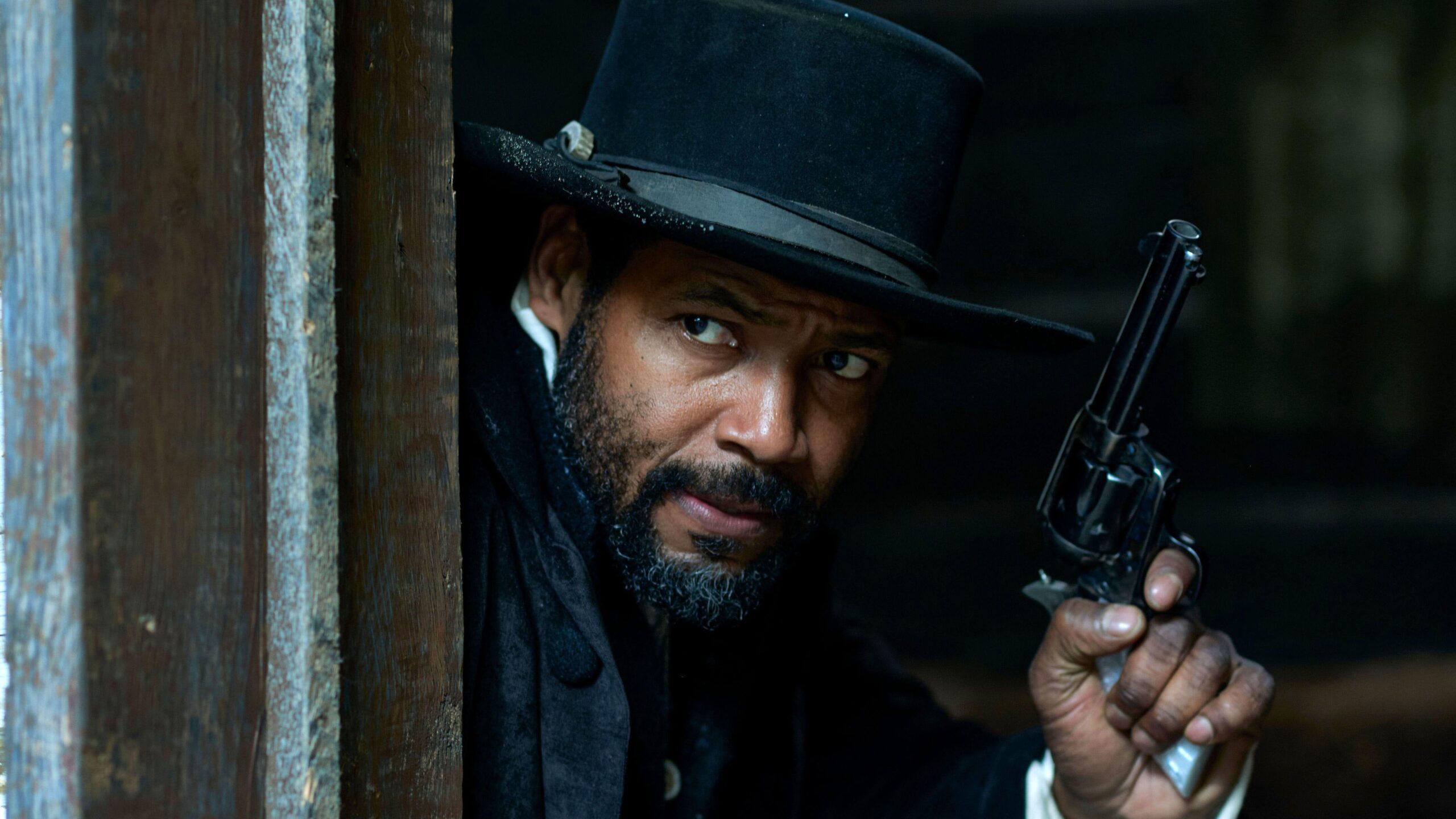 Cicero (Isaiah Mustafa) peers round a door frame, gun readied, in a scene from "Murder at Yellowstone City"