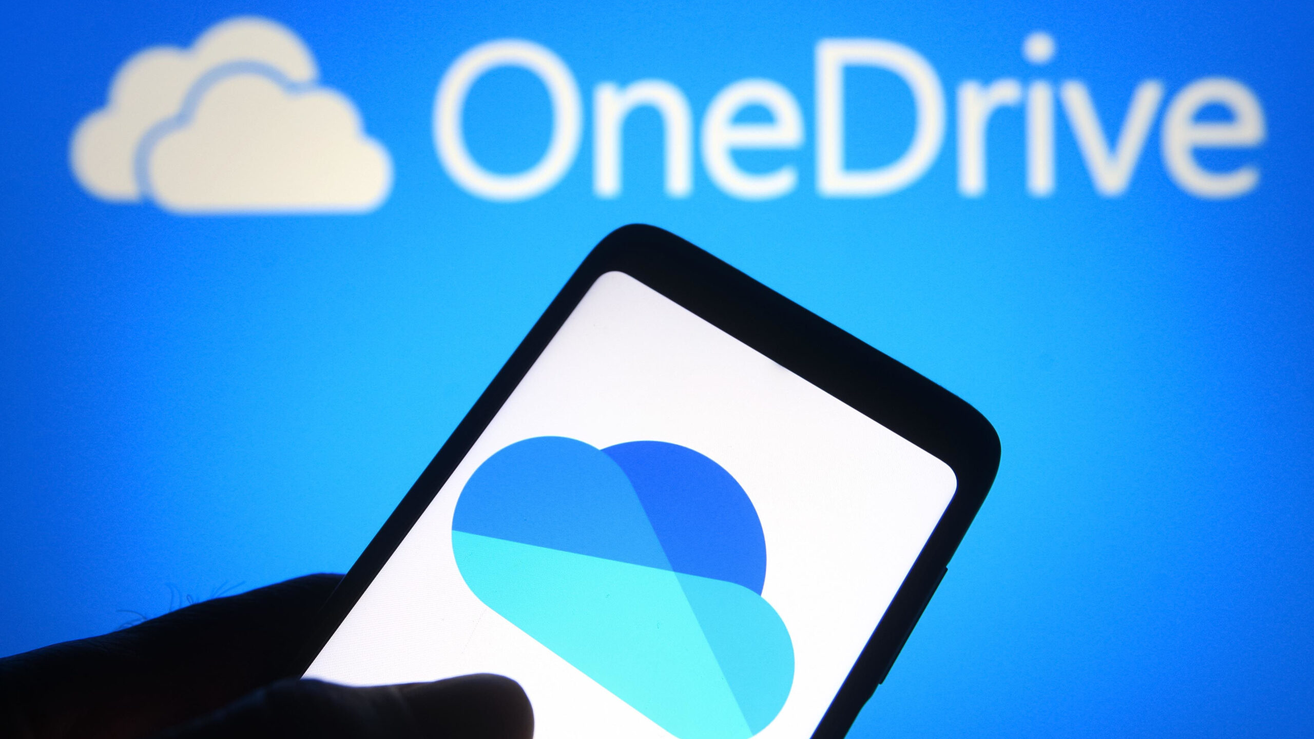The Microsoft OneDrive logo on a smartphone in front of the service's branding on a blue wall