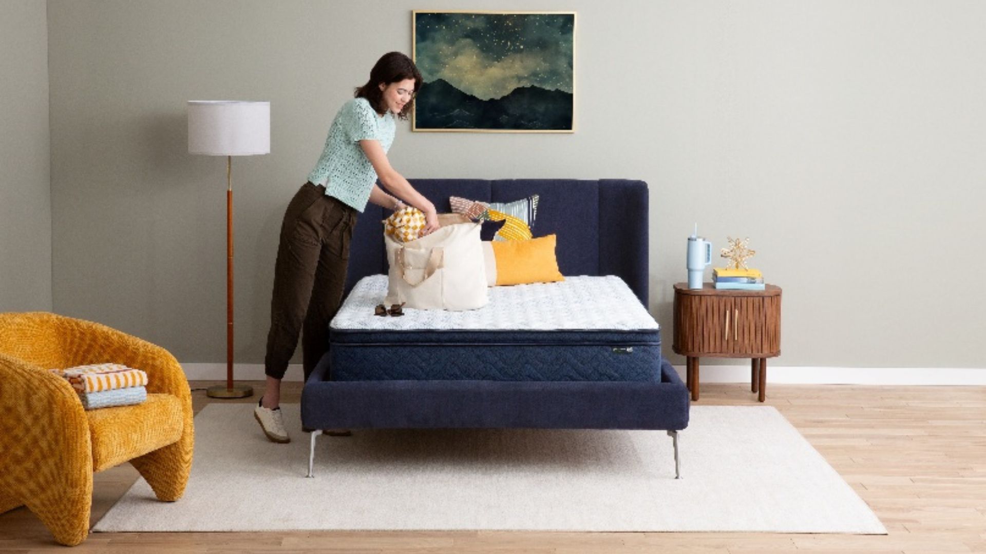 A brunette women looks through a beige tote bag that rests on the new Serta Five Star Mattress in a clean, well-lit bedroom.